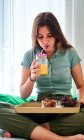 Jeune femme dégustant un petit déjeuner sain avec des baies fraîches et du jus tout en étant assis avec les jambes croisées sur le lit le matin — Photo de stock