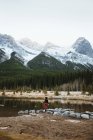 Back view of unrecognizable female hiker standing alone on shore of Quarry Lake against majestic forested mountains with snow covered rocky peaks in Banff National Park in Canada — Stock Photo