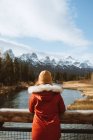Vue arrière d'une randonneuse méconnaissable portant des vêtements de dessus sur un pont qui contemple des paysages étonnants avec des montagnes enneigées et des forêts de conifères le jour de l'automne dans le parc national Banff au Canada — Photo de stock