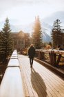 Visão traseira do viajante masculino irreconhecível na passarela de madeira contra a paisagem montanhosa com picos cobertos de neve enquanto passa férias de outono na cidade de Canmore, perto do Parque Nacional de Banff, no Canadá — Fotografia de Stock