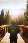 Back view of unrecognizable male traveler on wooden footbridge against mountainous landscape with snow covered peaks while spending autumn holidays in town of Canmore near Banff National Park in Canada — Stock Photo