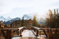 Malerische herbstliche Landschaft mit Brücke und Holzhäusern in Flussnähe gegen verschneite Berge in der Stadt Canmore in der Nähe des Banff National Park in Kanada — Stockfoto
