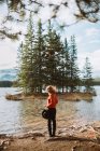 Visão traseira da fêmea irreconhecível em pé admirando árvores de coníferas verdes crescendo em ilhotas no meio do lago Two Jack contra o céu azul nublado em Alberta, Canadá — Fotografia de Stock