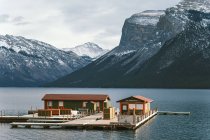 Dock with sheds floating on water of lake Minnewanka against snowy mountain range in Alberta, Canada — Stock Photo