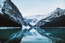 Чистая вода мирного озера Луиза отражает снежный горный хребет и облачное небо в зимний день в Альберте, Канада — стоковое фото