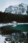 Wooden hut located on coast of calm Lake Louise near coniferous forest and snowy mountain on winter day in Alberta, Canada — Stock Photo