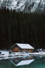 Cabana de madeira localizada na costa nevada de calma Lago Louise perto de floresta de coníferas e cume de montanha no dia de inverno frio no Parque Nacional de Banff — Fotografia de Stock