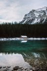 Wooden hut located on coast of calm Lake Louise near coniferous forest and snowy mountain on winter day in Alberta, Canada — Stock Photo