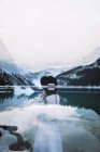Dupla exposição de fêmea sonhadora irreconhecível em vestido e chapéu descansando perto do Lago Louise e montanhas nevadas no dia de inverno no Parque Nacional de Banff — Fotografia de Stock