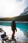 Full body anonymous traveler in outerwear standing on rocks near calm water of Lake Louise in morning in Banff National Park — Stock Photo