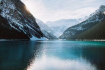 Sauberes Wasser des friedlichen Lake Louise spiegelt den schneebedeckten Bergrücken und den bewölkten Himmel an einem Wintertag in Alberta, Kanada — Stockfoto
