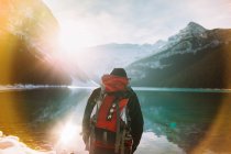 Blick zurück auf einen anonymen Wanderer mit Rucksack, der an einem sonnigen Wintermorgen im Banff National Park gegen den ruhigen Lake Louise und die verschneiten Berge wandert — Stockfoto