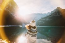 Rückansicht einer anonymen Wanderin in warmer Kleidung, die an einem sonnigen Wintermorgen im Banff National Park gegen den ruhigen Lake Louise und die stehenden Berge spaziert — Stockfoto
