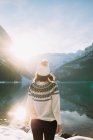 Vista trasera de una excursionista anónima con ropa de abrigo caminando contra el tranquilo lago Louise y montañas de pie en la soleada mañana de invierno en el Parque Nacional Banff - foto de stock