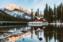 Довгий міст перетинає Емеральд озеро біля дерев'яного котеджу, розташованого біля хвойних лісів і сніжної гори в зимовий день у Британській Колумбії (Канада). — стокове фото