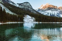 Acqua pulita del tranquillo lago di smeraldo che riflette cresta di montagna innevata e cielo nuvoloso nella giornata invernale in Alberta, Canada — Foto stock