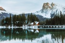 Довгий міст перетинає Емеральд озеро біля дерев'яного котеджу, розташованого біля хвойних лісів і сніжної гори в зимовий день у Британській Колумбії (Канада). — стокове фото