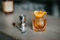 Composizione di whisky freddo ghiacciato guarnito con fetta di limone e posto sul tavolo di cemento vicino al jigger — Foto stock