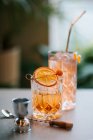 Zusammensetzung aus kaltem, eisigem Whisky, garniert mit Orangenscheiben und platziert auf einem Betontisch in der Nähe von Jigger und süßem Cocktail mit Stroh — Stockfoto