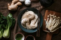 Vista superior de ingredientes variados para una sabrosa preparación de ramen colocada sobre un mantel marrón en la cocina. - foto de stock