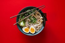 Top view of ceramic bowl with delicious ramen and chopsticks placed on red background — Stock Photo