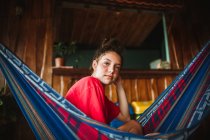 Side view of serene young female traveler in bikini looking at camera chilling in hammock hanging on terrace of tropical house during summer holidays in Uvita town in Costa Rica — Stock Photo