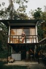 Von unten steht eine junge langhaarige Reisende in stylischer Badebekleidung auf dem Balkon eines Strandhauses in der Nähe grüner Bäume an einem Sommertag in der Stadt Uvita in Costa Rica — Stockfoto