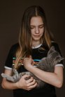 Мечтательная девочка-подросток держит пушистую милую кошку на коричневом фоне в студии — стоковое фото