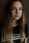 Encantadora menina adolescente com cabelos longos olhando para a câmera no fundo escuro em estúdio — Fotografia de Stock