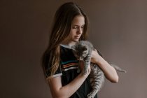 Adolescente rêveuse tenant un chat mignon moelleux sur fond brun en studio — Photo de stock