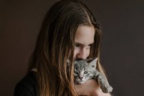 Задумчивая девочка-подросток с пушистым милым котом на коричневом фоне в студии — стоковое фото