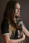 Rêveuse adolescente réfléchie tenant le chat mignon moelleux sur fond brun en studio — Photo de stock