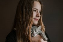 Dreamy thoughtful teenage girl holding fluffy cute cat on brown background in studio — Stock Photo