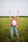 Happy young female standing in meadow in summer and showing rock sign while looking at camera — Stock Photo