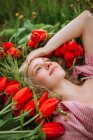 Visão superior da fêmea positiva deitada no campo com flores de tulipa vermelha e olhando para longe — Fotografia de Stock