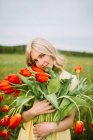 Contenuto femminile in abito in piedi con mazzo di fiori di tulipano rosso nel prato in estate — Foto stock