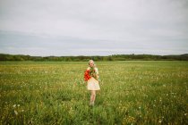 Conteúdo fêmea de vestido em pé com um monte de flores vermelhas de tulipa no prado no verão — Fotografia de Stock