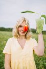 Ніжна жінка вкриває око червоною квіткою тюльпанів, стоячи на полі і дивлячись на камеру — стокове фото