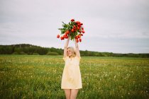 Усміхнена чарівна жінка з букетом червоних квітів тюльпанів, що сидить на зеленому лузі влітку — стокове фото