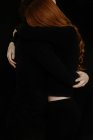 Unrecognizable side view of cropped tender boyfriend tenderly embracing redhead girlfriend while standing in dark studio on black background — Stock Photo