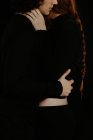 Невідомий вид збоку обрізаного ніжного хлопця, ніжно захоплюючи руду дівчину, стоячи в темній студії на чорному тлі — стокове фото