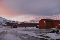 Maisons résidentielles rouges situées dans la vallée enneigée dans les hautes terres en hiver sur fond de ciel couchant à Svalbard — Photo de stock