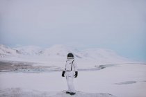 Unrecognizable cosmonaut wearing white spacesuit standing on snowy field in winter and admiring amazing landscape in Svalbard — Stock Photo