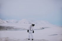 Unerkennbarer Kosmonaut in weißem Raumanzug, der im Winter auf einem verschneiten Feld steht und die atemberaubende Landschaft in Spitzbergen bewundert — Stockfoto