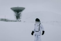 Unrecognizable cosmonaut in spacesuit standing in snowy valley in winter on background of huge radar antennas in Svalbard — Stock Photo