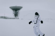 Unrecognizable cosmonaut in spacesuit standing in snowy valley in winter on background of huge radar antennas in Svalbard — Stock Photo