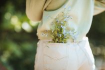 Vue arrière de l'adolescente cultivée avec des fleurs sauvages dans la poche du jean debout dans le parc d'été — Photo de stock
