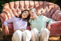 Sanfte Teenie-Schwestern sitzen an sonnigen Tagen neben einer bequemen Couch im Garten und schauen in die Kamera — Stockfoto