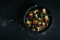 Ensalada vegetariana de arriba con tofu frito y verduras servidas sobre fondo negro - foto de stock