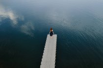 Зверху віддалений вид жінки, що стоїть на краю набережної біля спокійного озера — стокове фото
